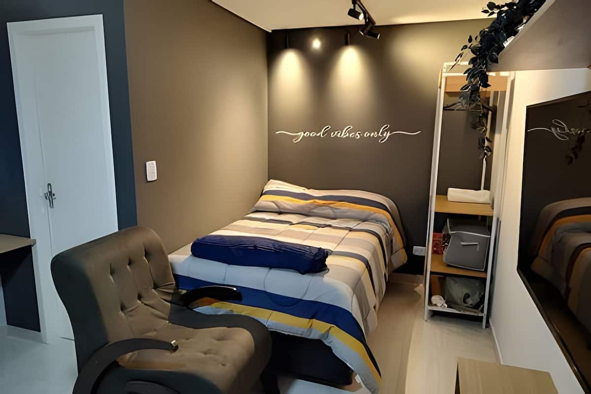 A bedroom with a bed, a chair, a wardrobe, and a wall with a motivational quote.
