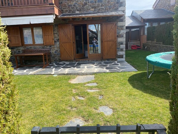 Enjoy a tranquil retreat with a stone patio, wooden door, and a backyard featuring a trampoline and grassy lawn.
