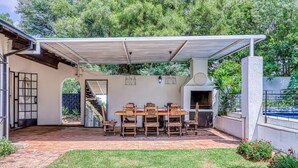 A covered patio with a dining table and chairs, a brick pathway, and a small garden area. - Chic Midtown Studio-1 Bed-solar-pool-fibre-samrand (Centurion)