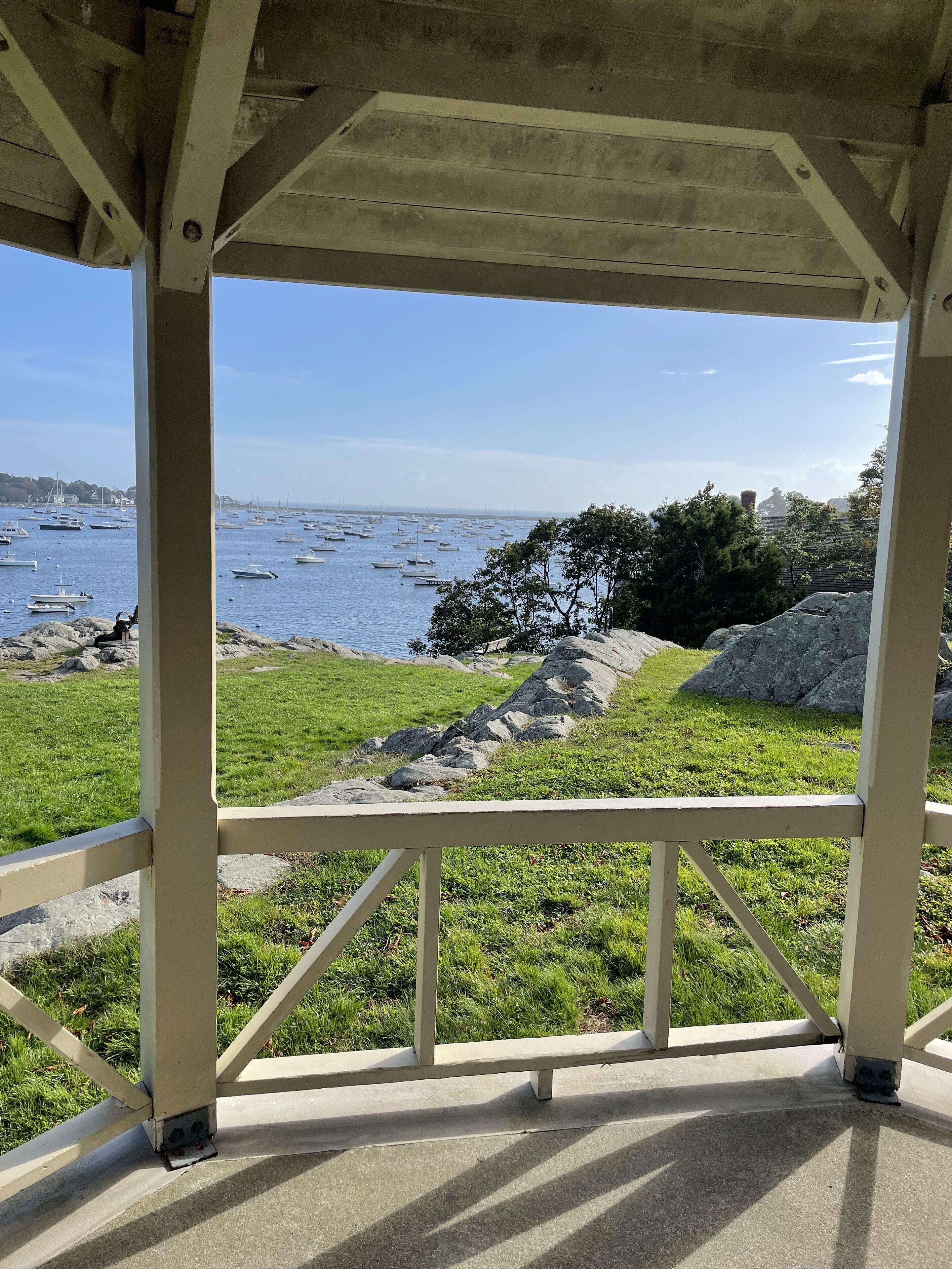 A gazebo with a view of a rocky shoreline and boats in the water.