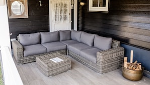 A sectional sofa and two wicker ottomans on a porch with a door and window. - Sfeervol Vakantiehuisje in het Charmante Yerseke (Yerseke)