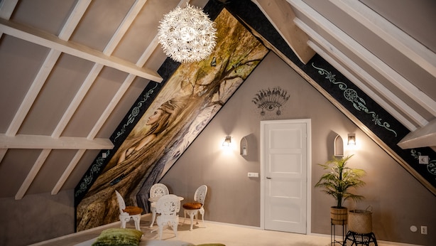 A bedroom with a sloped ceiling, a bed with green pillows, a white chair, a small table, a potted plant, and a decorative wall piece. - Sfeervol Vakantiehuisje in het Charmante Yerseke (Yerseke)