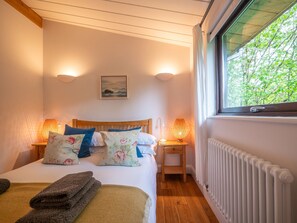 Une chambre Ă coucher avec un lit en bois, deux lampes de chevet, un radiateur et une fenĂȘtre donnant sur des arbres.