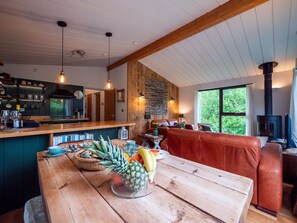 Un tavolo da pranzo in legno con frutta, un angolo cottura con piano cottura e un'area salotto con divano in pelle.
