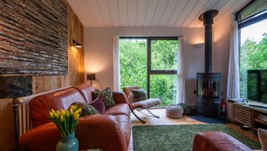 Una sala de estar acogedora con un sofá de cuero, una chimenea y un ventanal con vistas a la vegetación.