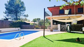 A swimming pool with a tiled deck, a grassy lawn, and a two-story building with a red facade and a balcony. - Morera Blanca (Canet de Fals)