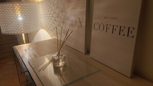 A modern table with a glass top, a clear glass bottle with reed sticks, and a lamp with a textured shade. - Morera Blanca (Canet de Fals)