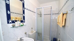 Et badeværelse med et glasafskærmet brusebad, en vask med toiletartikler og en håndklædestang.