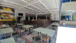 An indoor dining area with multiple tables and chairs, a counter with a bartender, and a large poster on the wall. - Golden Dolphin 01 Quarto - Caldas Novas -GO (Caldas Novas)