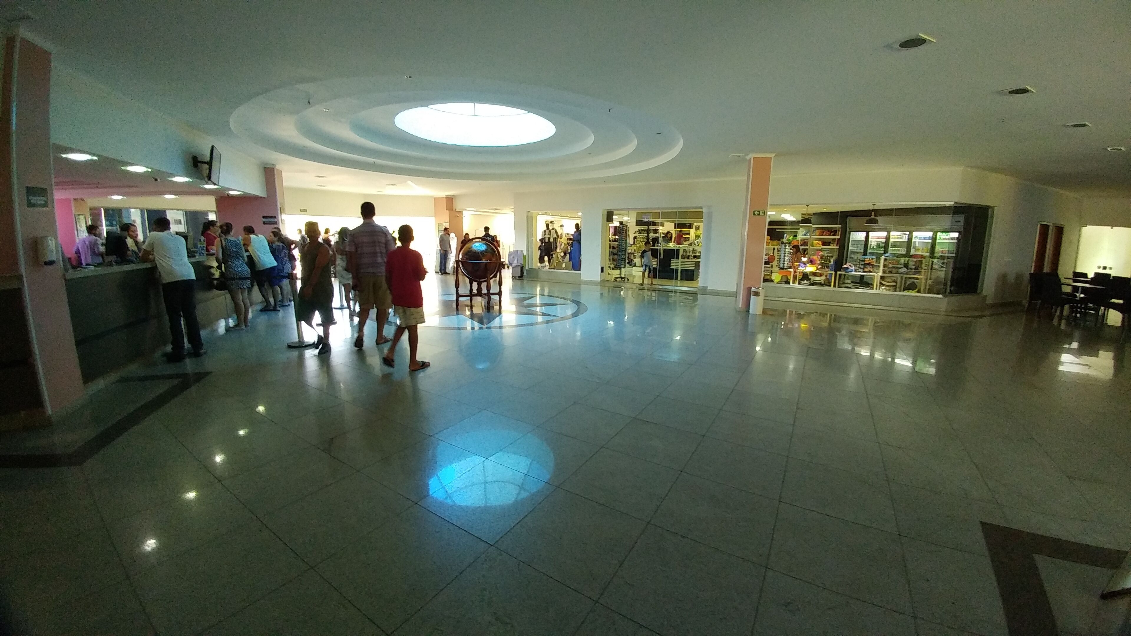A spacious indoor area with a central circular skylight, tiled floors, and various shops and seating areas.