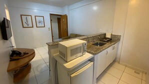 A compact kitchen with a microwave, sink, and a small refrigerator. There is a wooden counter and a door leading to another room. - Golden Dolphin 01 Quarto - Caldas Novas -GO (Caldas Novas)