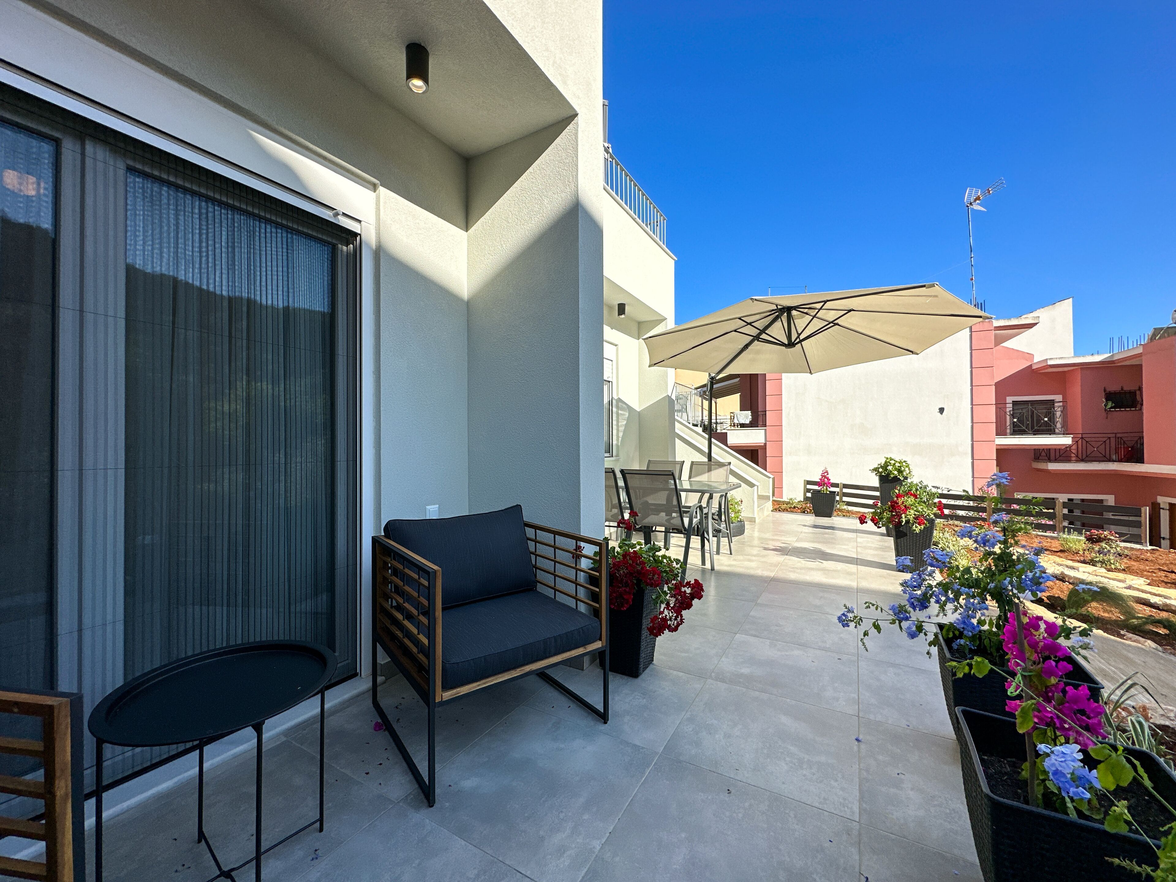 An outdoor patio with a sofa, chairs, and a table. There are potted plants and a large umbrella.