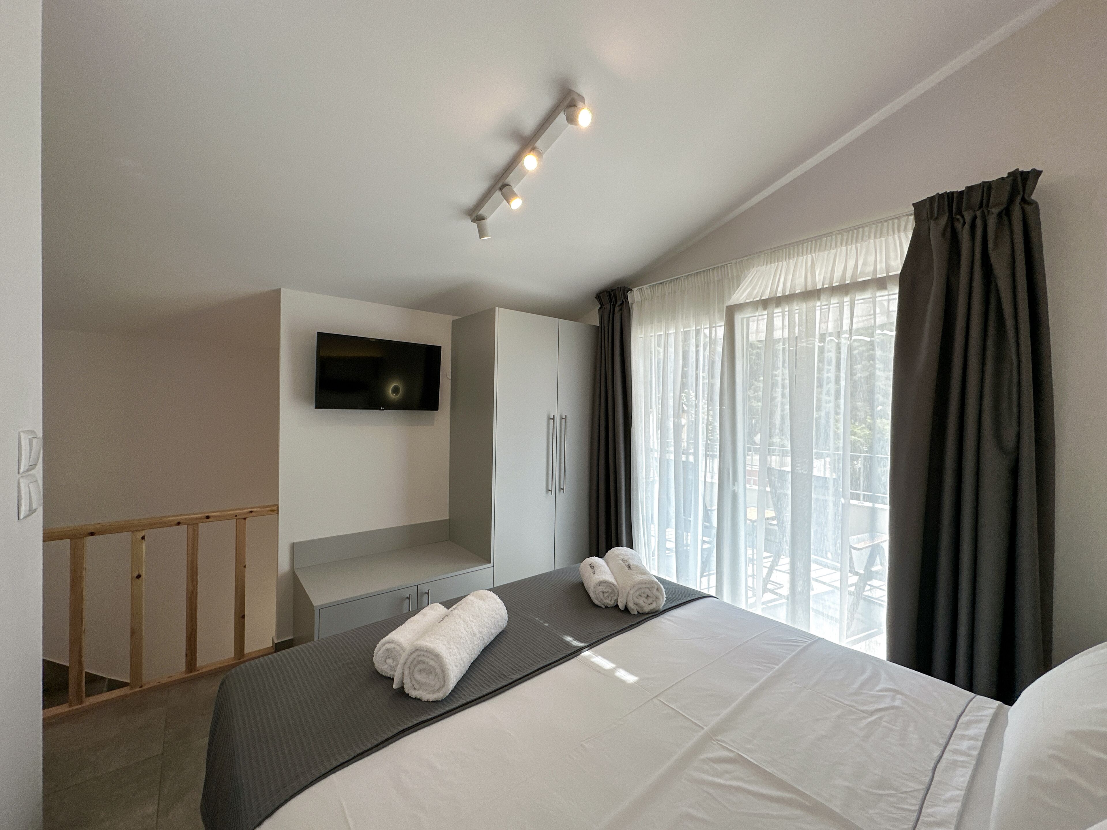 Quarto de hotel com cama, televisão na parede, janela com cortinas e luminária no teto.