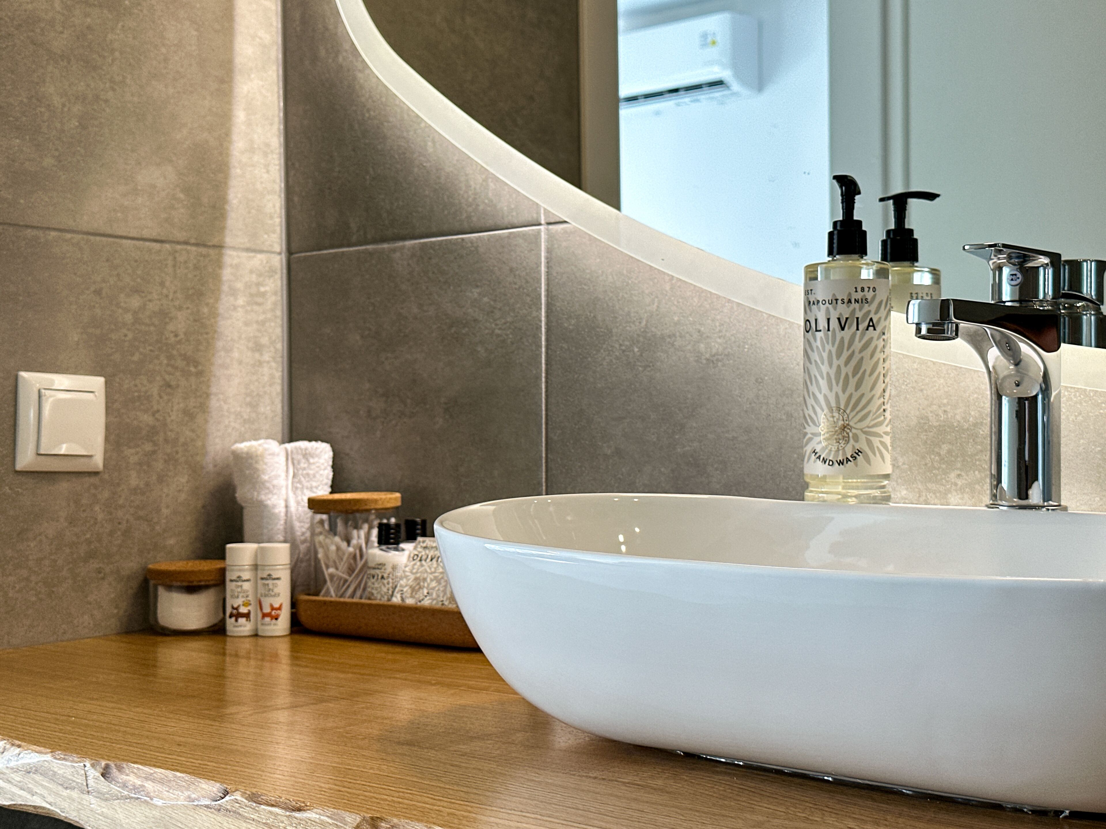 Ein Badezimmer mit weißem Waschbecken, einem Spiegel und Toilettenartikeln auf der Ablagefläche.