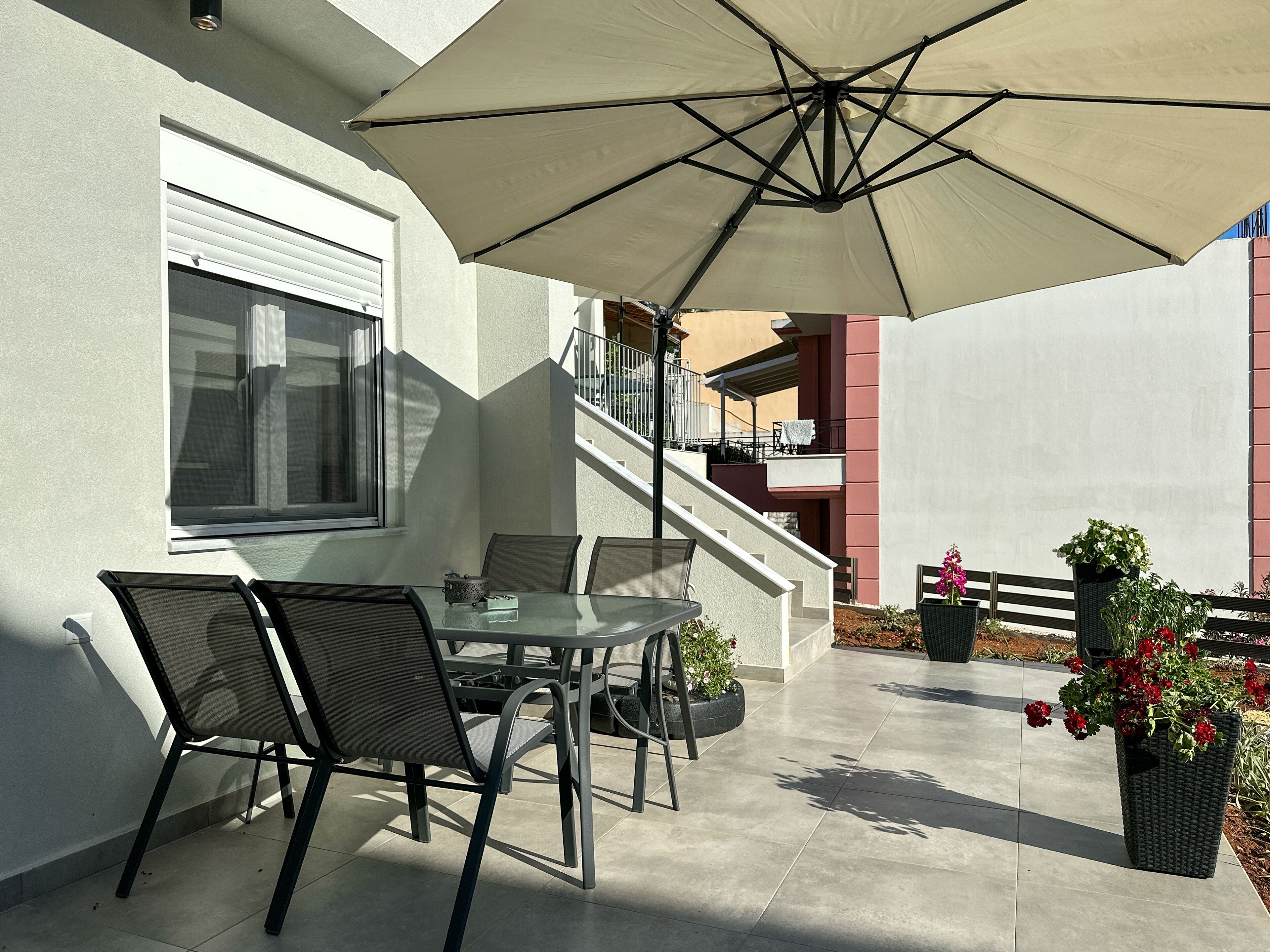 Eine Terrasse im Freien mit Tisch, Stühlen, einem großen Sonnenschirm und Blumentöpfen.