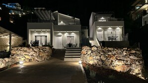 Una casa moderna de dues plantes amb façana de pedra, una escala que condueix al pis superior i il·luminació exterior.