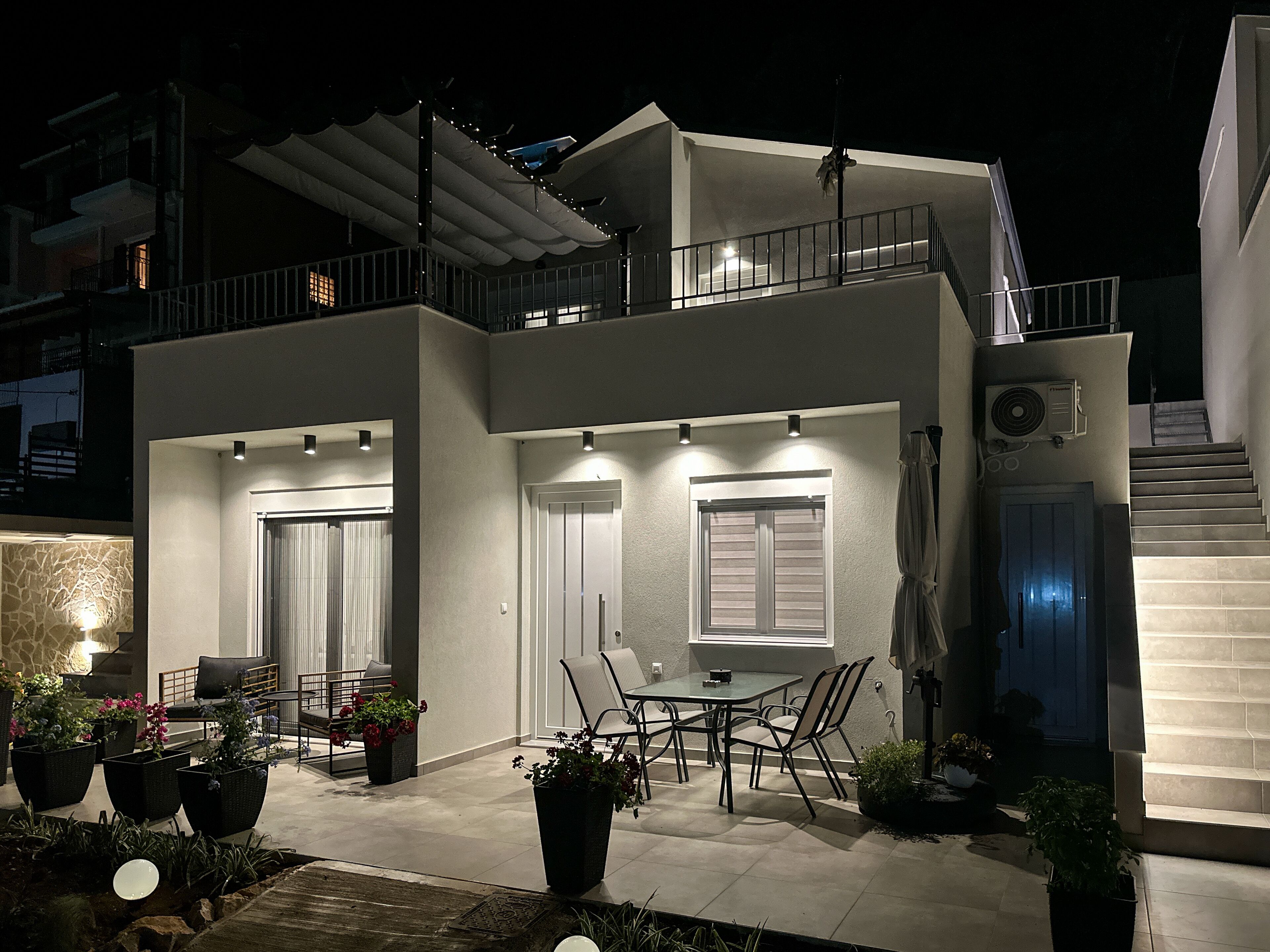 Una casa moderna de dos pisos con balcón, zona de estar al aire libre y una escalera que conduce al piso superior.