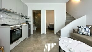 Una cuina moderna amb forn i fogó integrats, una zona de menjador amb taula de marbre, i una escala que condueix a un dormitori.
