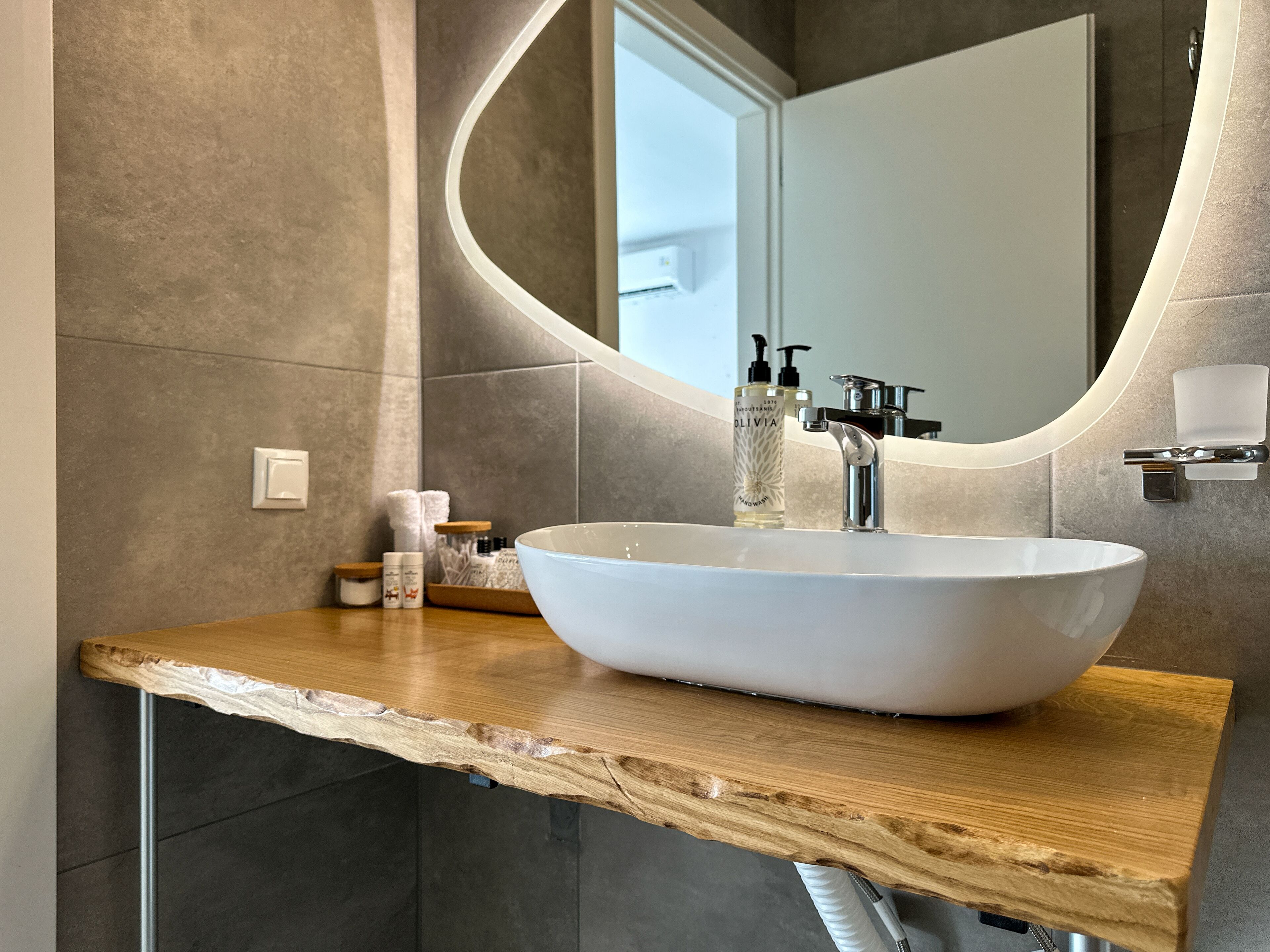 A bathroom with a white vessel sink, a wooden countertop, a large mirror, and a towel rack.