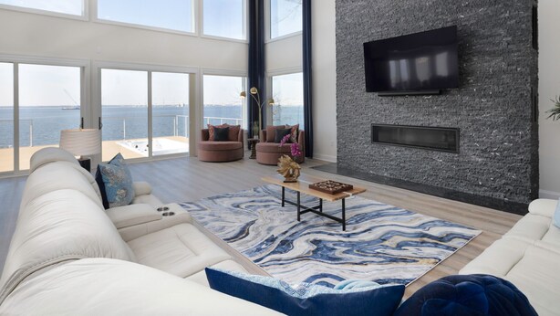 Amplia sala de estar con un ventanal que da a una extensión de agua, chimenea moderna y un televisor de pantalla plana montado en una pared con textura.