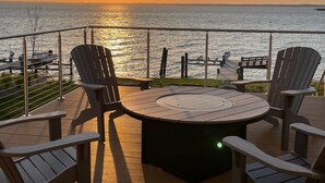 Terraza con una mesa redonda y cuatro sillas Adirondack con vista a un cuerpo de agua al atardecer.