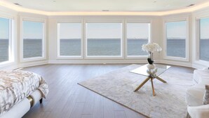 Un dormitorio espacioso con ventanas amplias, una cama, una mesita de centro de cristal y vistas al mar.