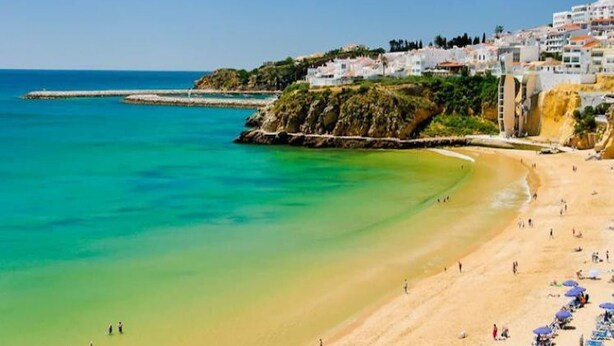 A coastal beach with clear turquoise waters, a sandy shore, and buildings in the background. - Albufeira 2 - Beach & Old Town (Albufeira)
