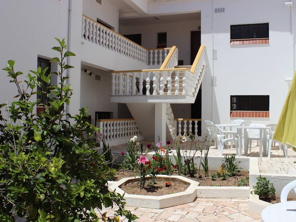 A multi-level courtyard with white railings, outdoor seating, and a garden area with various plants and flowers.
