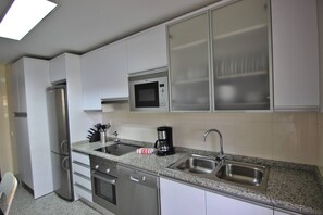 A modern kitchen with white cabinets, stainless steel appliances, a microwave, a coffee maker, and a sink. - Monte Laguna - Luxury Condominium (Vilamoura)