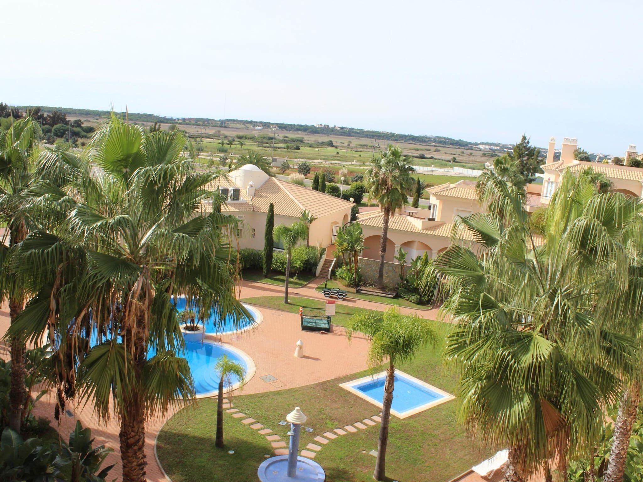 Ein Resort mit Swimmingpool, Palmen und Gebäuden im mediterranen Stil.