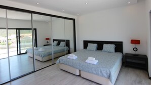 A modern bedroom with a large bed, a nightstand, a mirror, and a view of the outdoors. - Villa Goncinha - Private Pool & BBQ (Loulé)