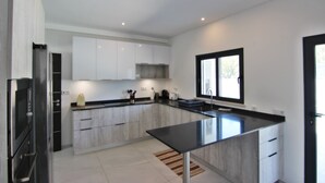 A modern kitchen with white cabinets, a black countertop, and a window providing natural light. - Villa Goncinha - Private Pool & BBQ (Loulé)