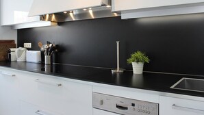 Et moderne køkken med hvide skabe, en sort bordplade, rustfrie stålemmer og en lille potteplante.