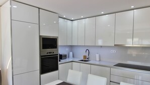 A modern kitchen with white cabinets, a built-in oven, a microwave, a sink, and a dining area with a table and chairs.