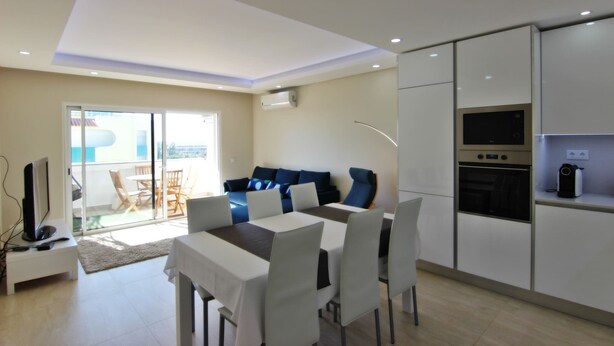 A modern living room with a dining area, a sofa, and a kitchen with a built-in oven.
