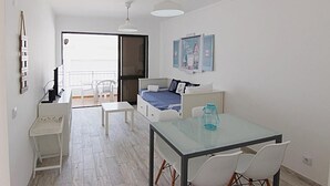 A bright, minimalist room with a bed, a small table, and a balcony.