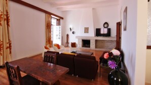 A spacious living room with a wooden dining table, sofas, and a fireplace. - Casa dos Tios - Sea View, Beach & Old Town Center (Albufeira)