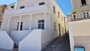 A white building with a staircase leading to the entrance, columns, and a balcony with potted plants. - Casa dos Tios - Sea View, Beach & Old Town Center (Albufeira)