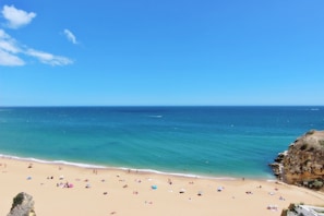 A beach with clear blue water, sandy shore, and rocky cliffs.