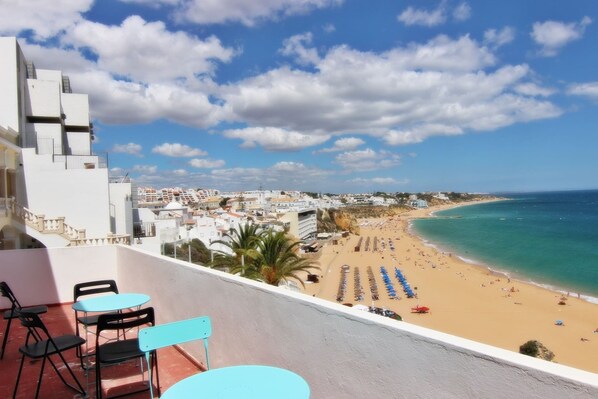 A balcony with outdoor seating overlooking a beach and cityscape.