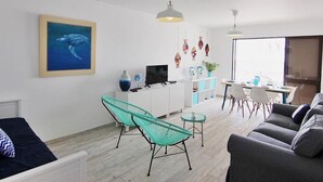 Una sala de estar moderna con un sofá, una mesa de vidrio y un televisor. Hay un cuadro en la pared y una planta sobre la mesa.