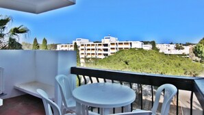 A balcony with a white table and chairs, overlooking a residential area with white buildings and greenery.