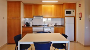A compact kitchen with wooden cabinets, a microwave, a refrigerator, and a dining table with chairs.