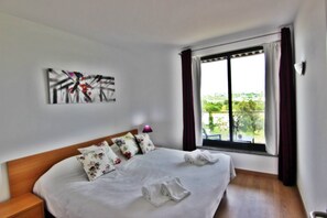 A hotel room with a bed, pillows, a painting on the wall, and a window with curtains.
