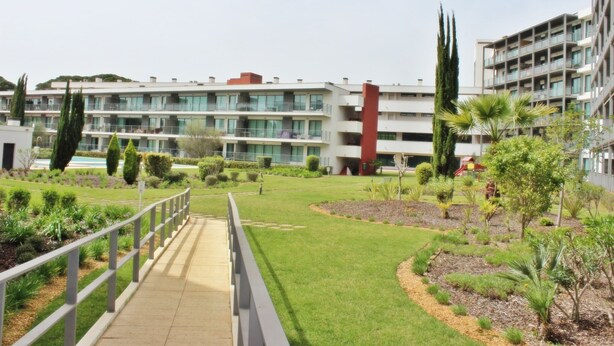 A modern building with multiple balconies, a well-maintained lawn, and a pedestrian bridge. - Residences Golf Club - Pool and Tenis Court (Vilamoura)