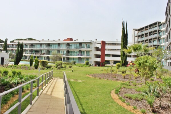 A modern building with multiple balconies, a well-maintained lawn, and a pedestrian bridge.