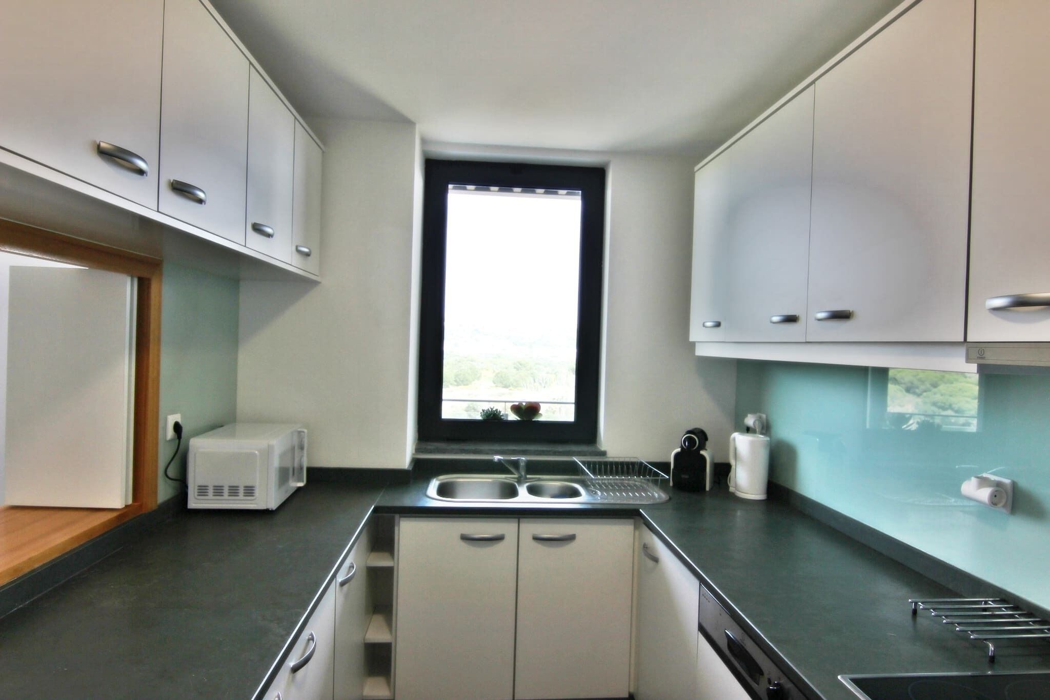 Una cocina moderna con ventana, electrodomésticos de acero inoxidable y encimera negra.