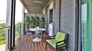 A balcony with a wooden floor, a round table with chairs, and a green cushioned chair. - Residences Golf Club - Pool and Tenis Court (Vilamoura)