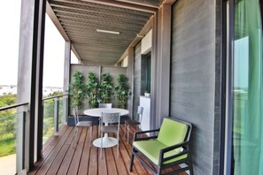 A balcony with a wooden floor, a round table with chairs, and a green cushioned chair.
