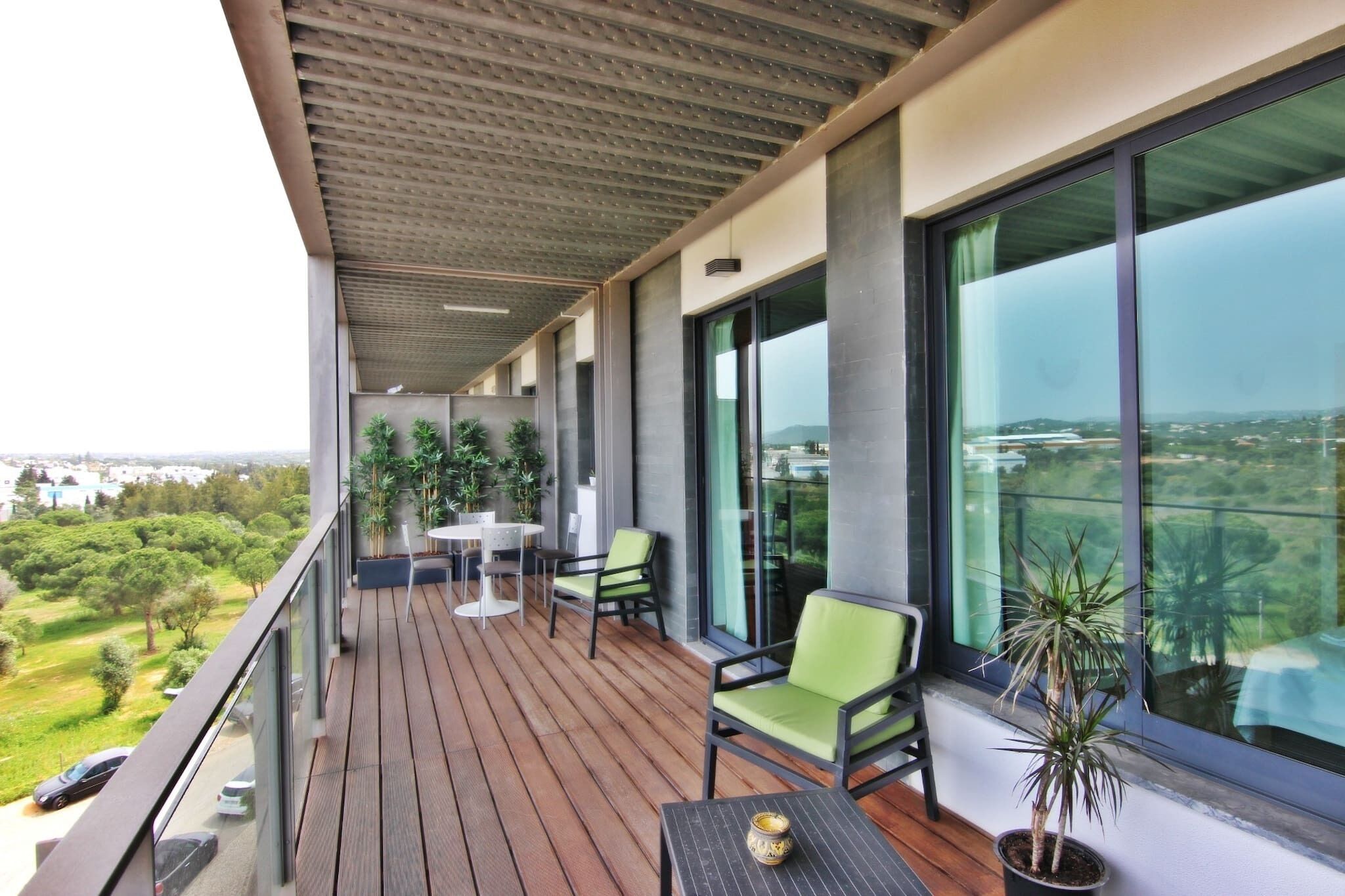 Un balcon avec un plancher en bois, une table, des chaises et des plantes en pot.